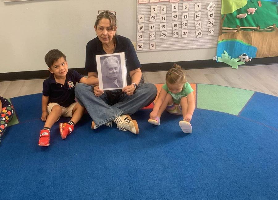 Una guía sostiene un retrato de María Montessori mientras una niña se pone sus zapatos